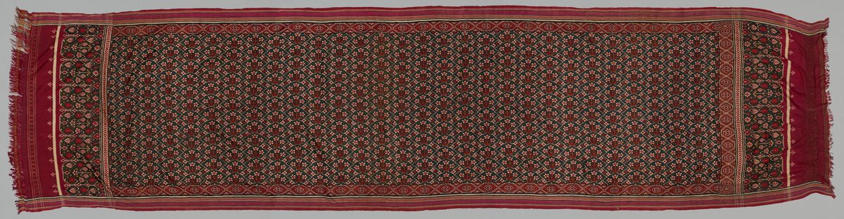 Full length of a red and dark green double-ikat patola sari, its field covered in small repeating floral lattice motifs between patterned end panels