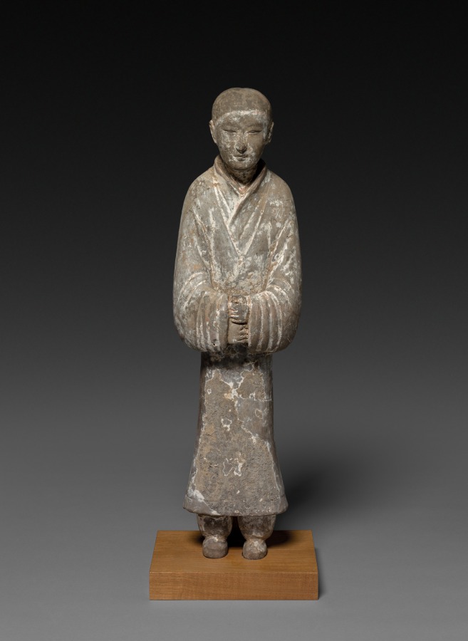 Clay tomb figurine of a Han dynasty attendant with hands clasped inside the long sleeves of a wrapped robe with layered collars