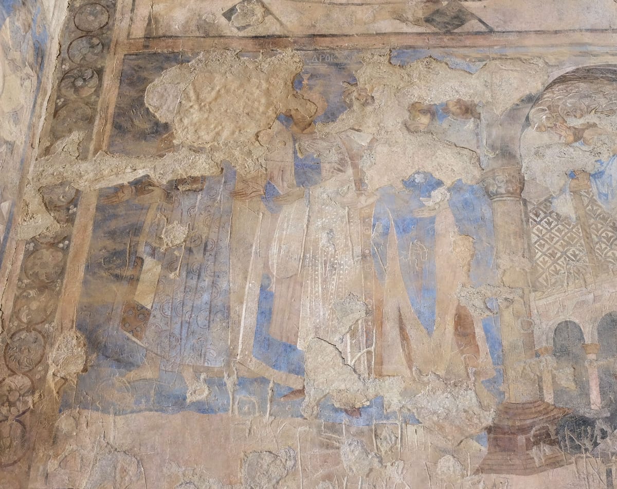 Damaged wall painting of a row of standing figures in long robes of blue, white, and red, with an arcade on the right