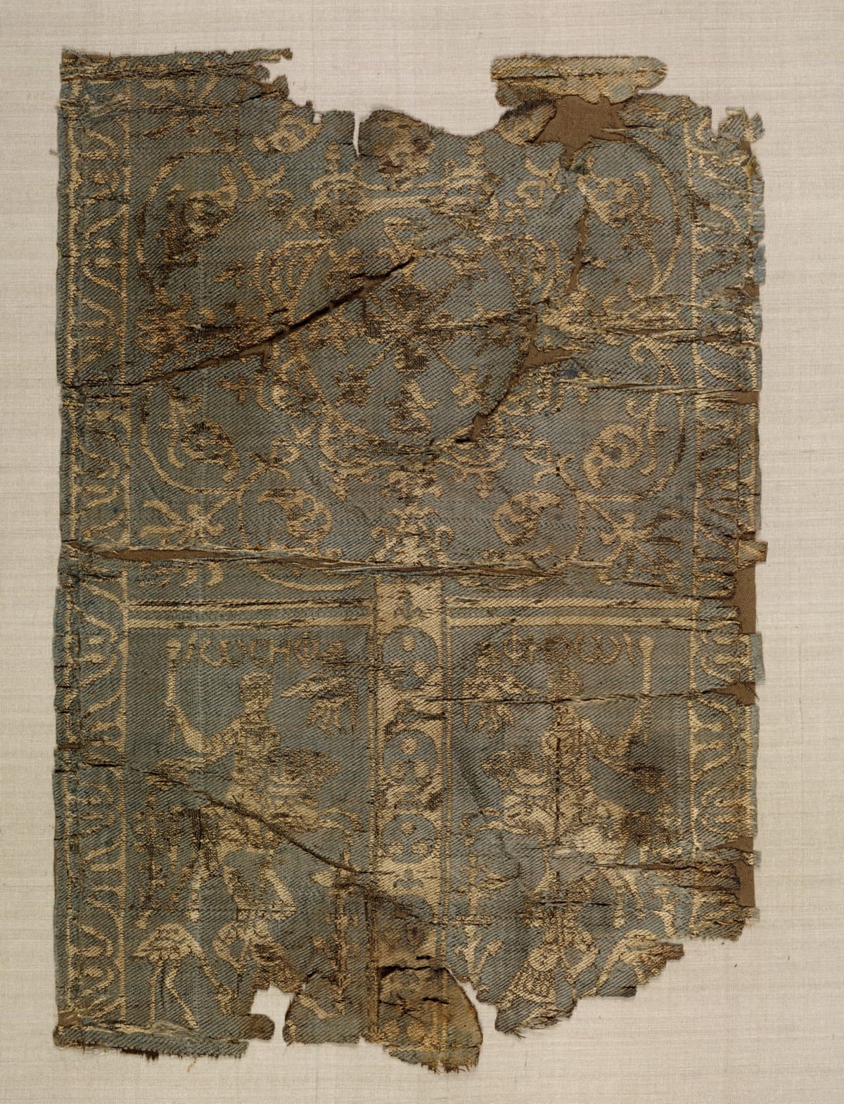 Silk sleeve panel in red, green, and cream, with a large leaf-and-palmette medallion above a horseman with a mace and small hunters with spears below