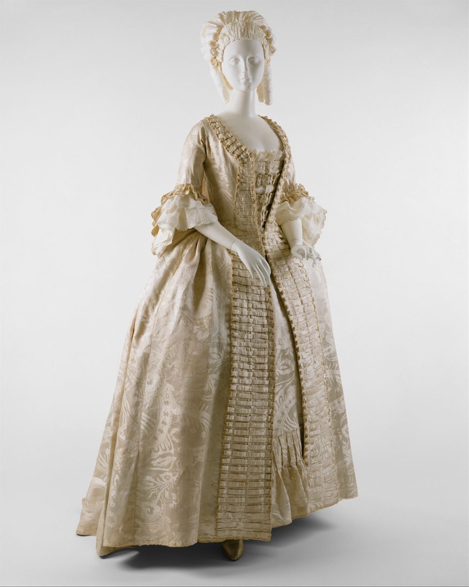A cream silk robe à la française with pleated trim and lace sleeve ruffles on a mannequin