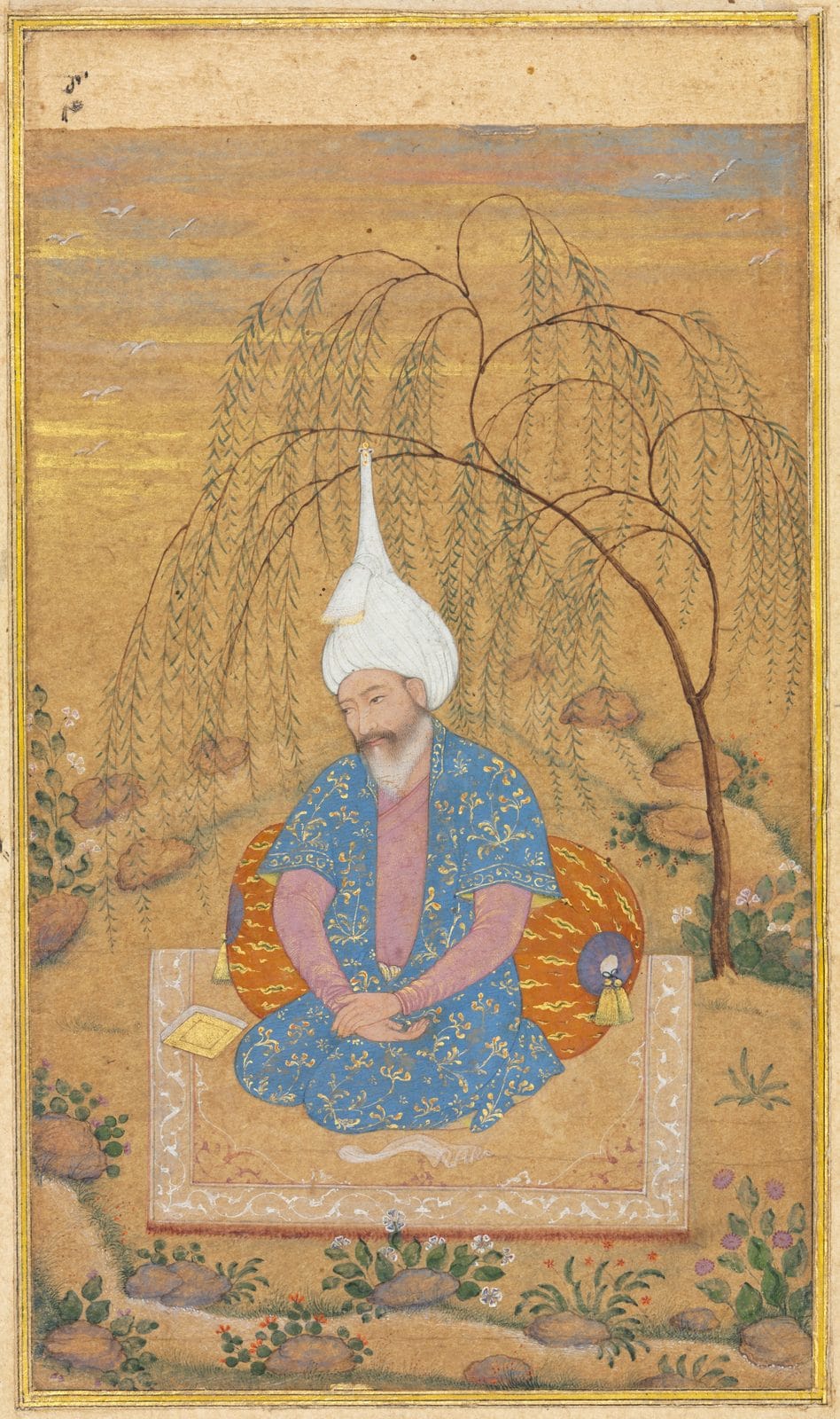 Persian miniature of Shah Tahmasp kneeling on a carpet under a willow, wearing a blue robe patterned in gold over a pink inner robe, and a white turban wound around a cap with a tall pointed baton rising from the top