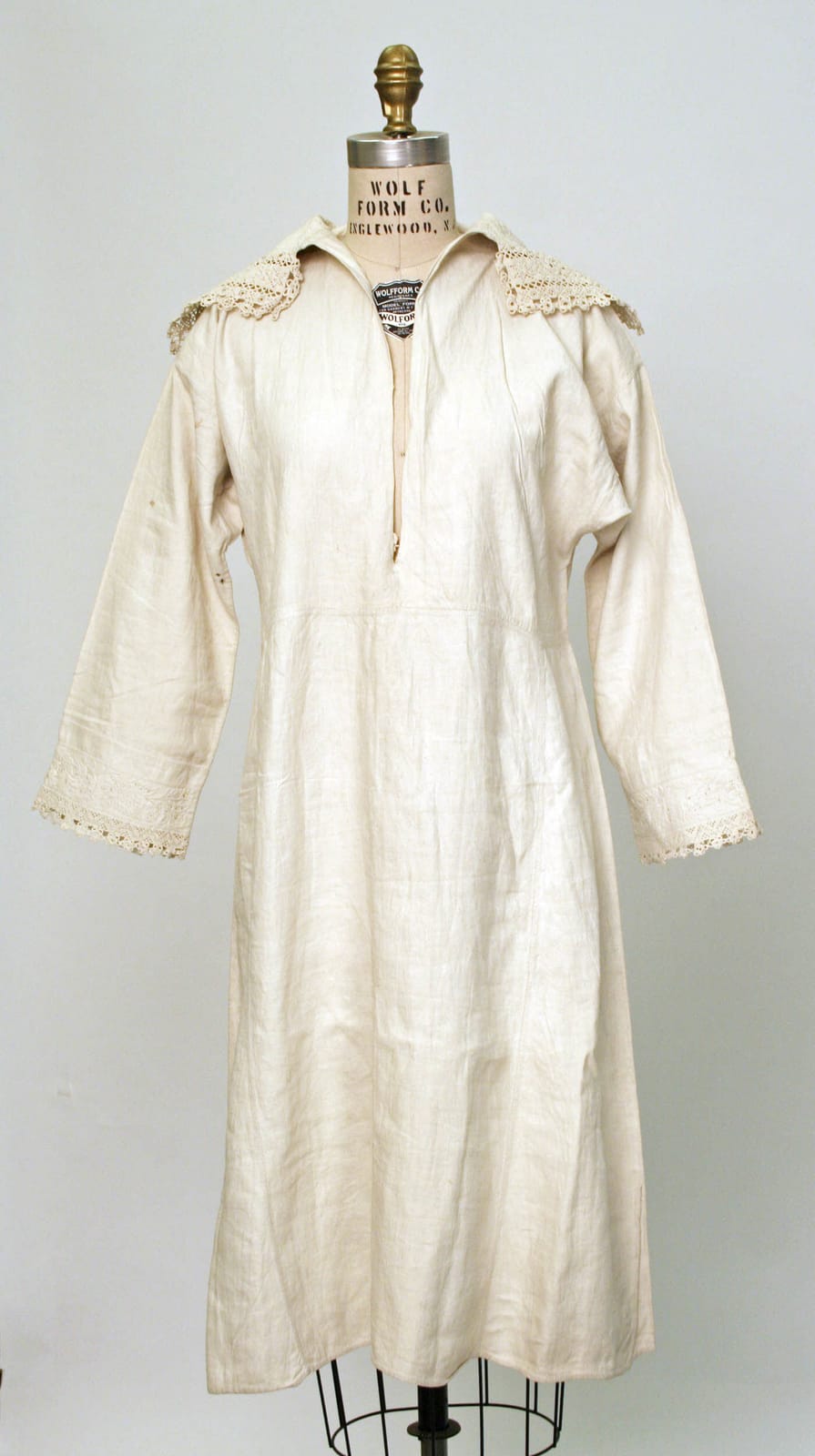 Long white linen chemise with long sleeves, a lace-trimmed collar, and a slit front opening, displayed on a dress form