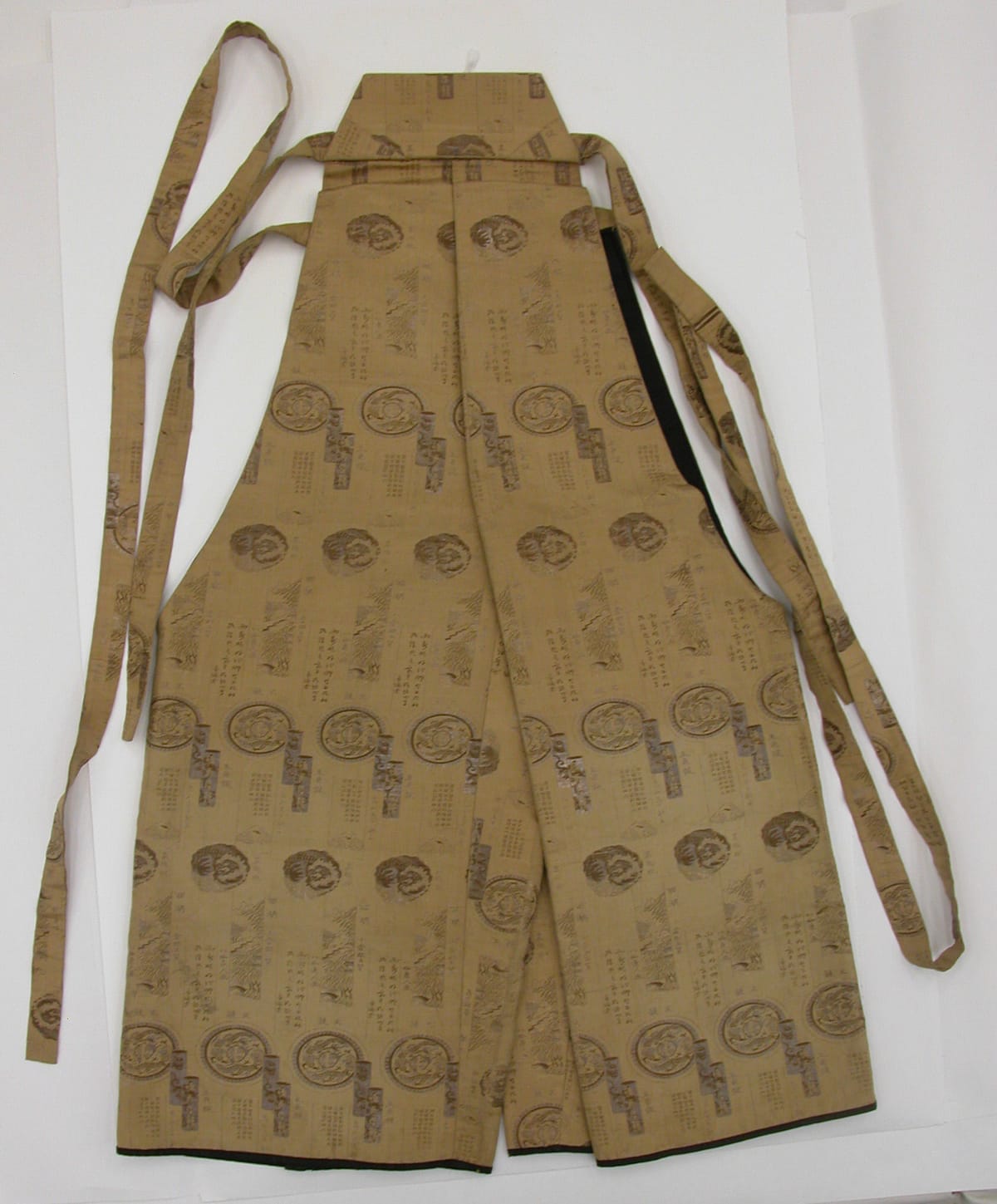 Pair of nineteenth-century Japanese hakama trousers of patterned tan silk, laid flat with long waist ties