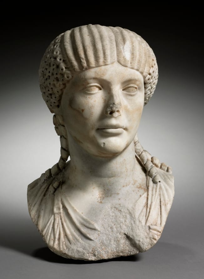 Marble portrait bust of a young Roman woman with an elaborate hairstyle, wearing a stola over her tunic