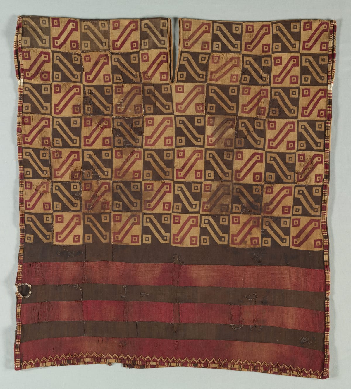 Inca man's tunic (unku) woven in tapestry, with a field of interlocking key motifs in red, gold, and dark brown above wide horizontal stripes