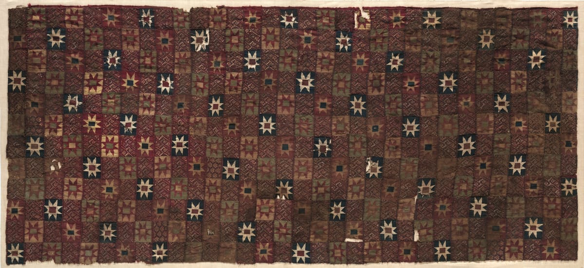 Long fragmentary Inca mantle in deep brown and red, patterned with a grid of squares, many holding white eight-pointed stars