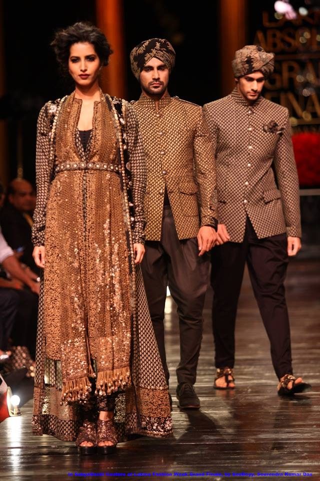 Models on a runway in Sabyasachi couture: a woman in a long embroidered coat over a flared skirt, and two men in patterned bandhgala jackets and turbans