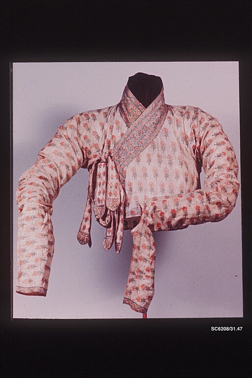Embroidered fragment of a Mughal jama bodice in pale cotton with rows of small red flowers, a wrapped crossover front, a patterned border at the neck, long gathered sleeves, and hanging tie strings