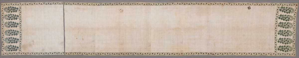 Long, narrow Mughal patka sash of fine white cotton with embroidered green flowering plants in a row of panels at each end and a narrow floral border along the edges
