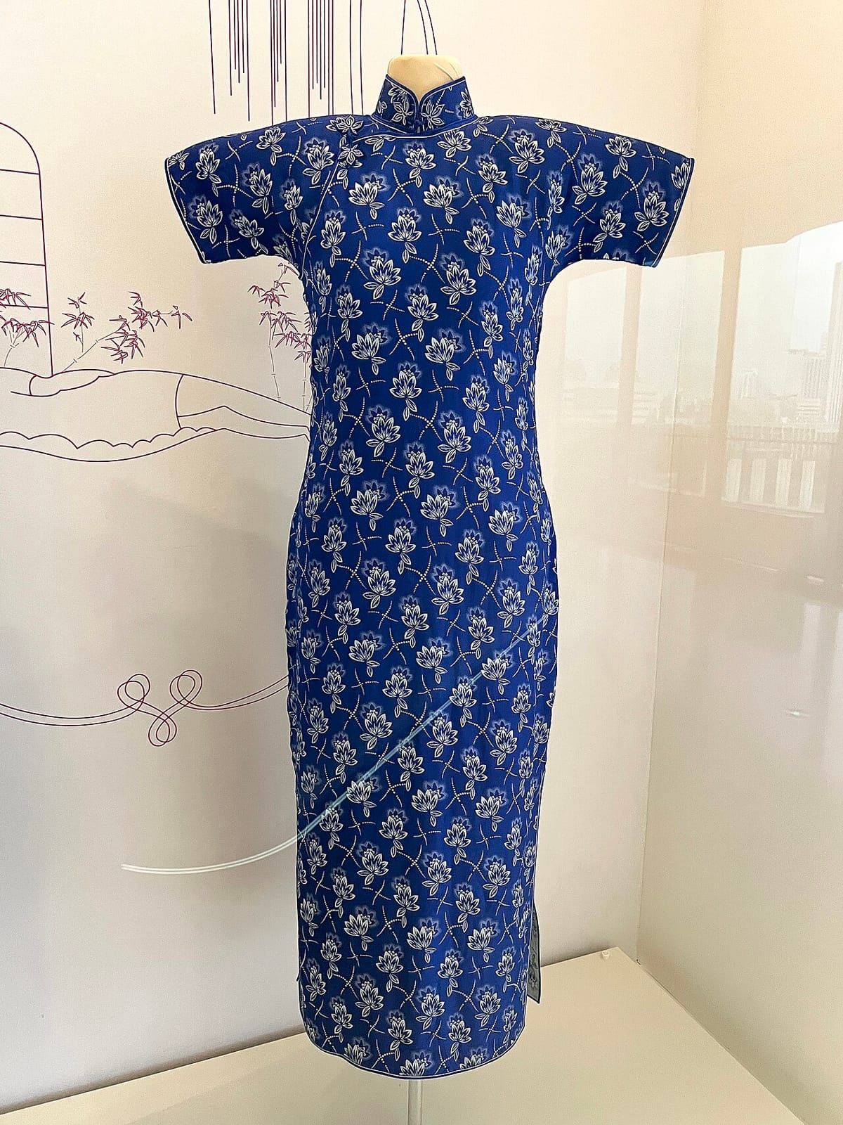 Short-sleeved, ankle-length blue qipao with a high collar and white floral print, displayed on a mannequin