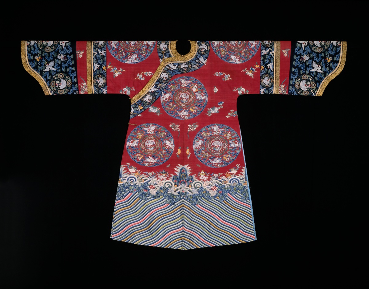 Red Qing dynasty woman's robe with a curved closure across the chest, wide sleeves with dark blue bands, roundels of white cranes, and a striped wave border at the hem
