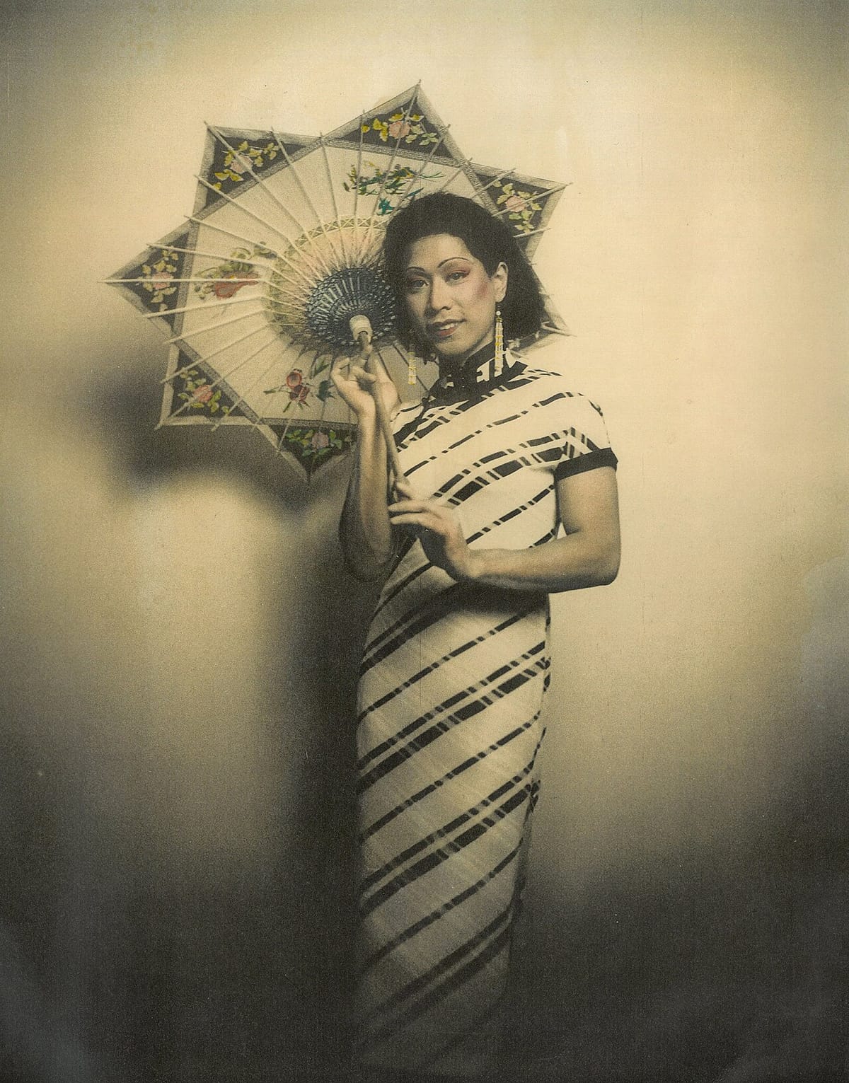 Hand-colored studio photograph of a woman in a long, close-fitting short-sleeved qipao with diagonal stripes, holding an open painted parasol