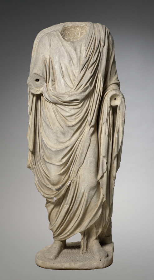 Headless marble statue of a man in a toga, with the folds falling to the feet and holes where the arms were attached
