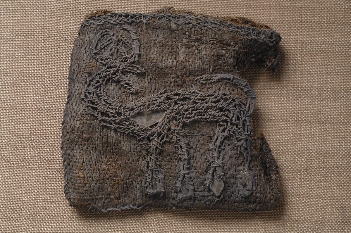 Square fragment of dark silk embroidered with silver thread in the outline of a stag turning its head