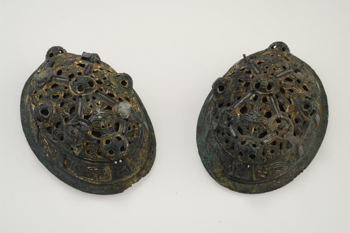 Pair of gilded bronze oval brooches with openwork domes, silver wire details, and green corrosion around the rims